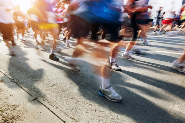 Marathon runners in motion. Running in the city, sun shining.