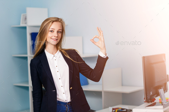 Young pretty business woman makes OK sign in blue office
