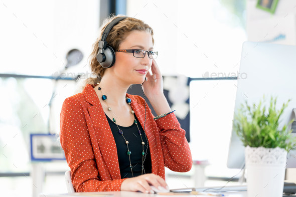 Young woman in casual clothes sitting in office in headphones