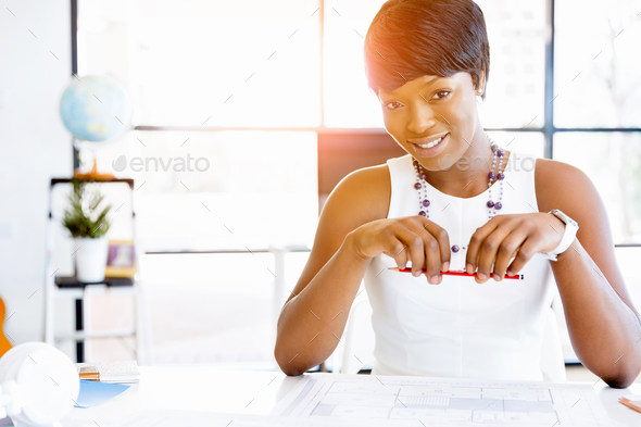Young beautiful woman sitting at a desk in an office and working on blueprint